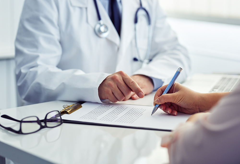 Female patient in office filling out medical document with docto