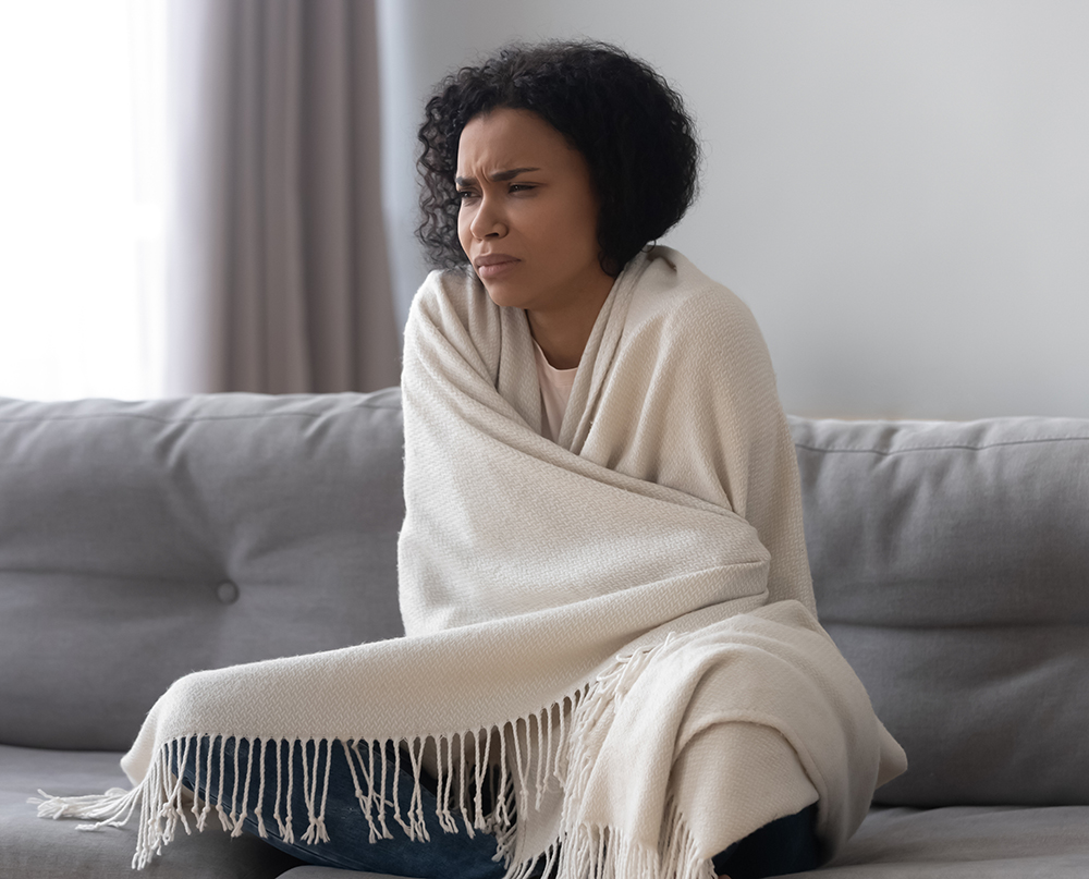 Unhappy African American woman feeling cold, covered with warm blanket