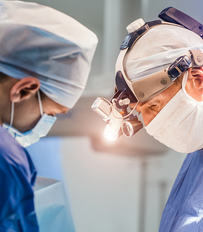 Two surgeons in operating room with surgery equipment and in binocular glasses.