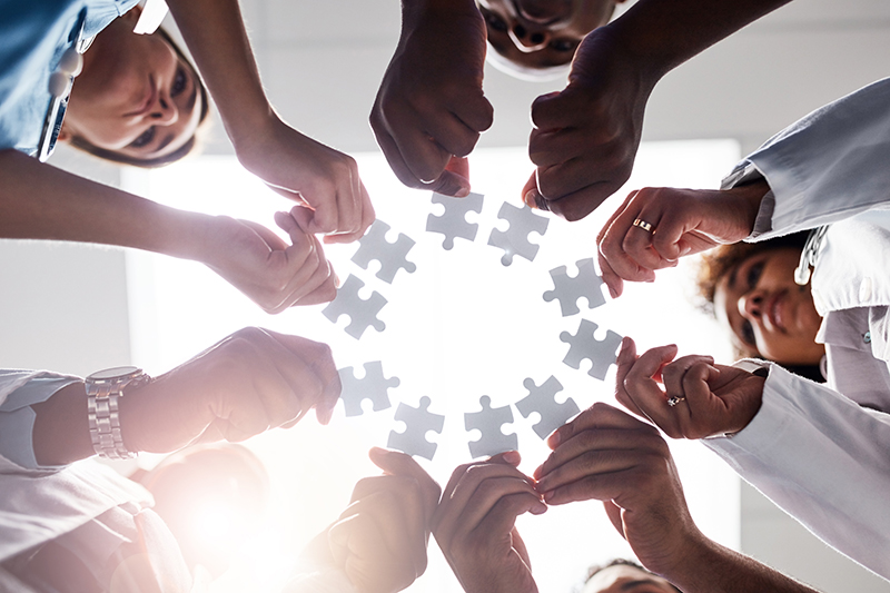Everyone plays their part here. Low angle shot of a group of doctors forming a huddle while each holds a puzzle piece inside of a hospital.