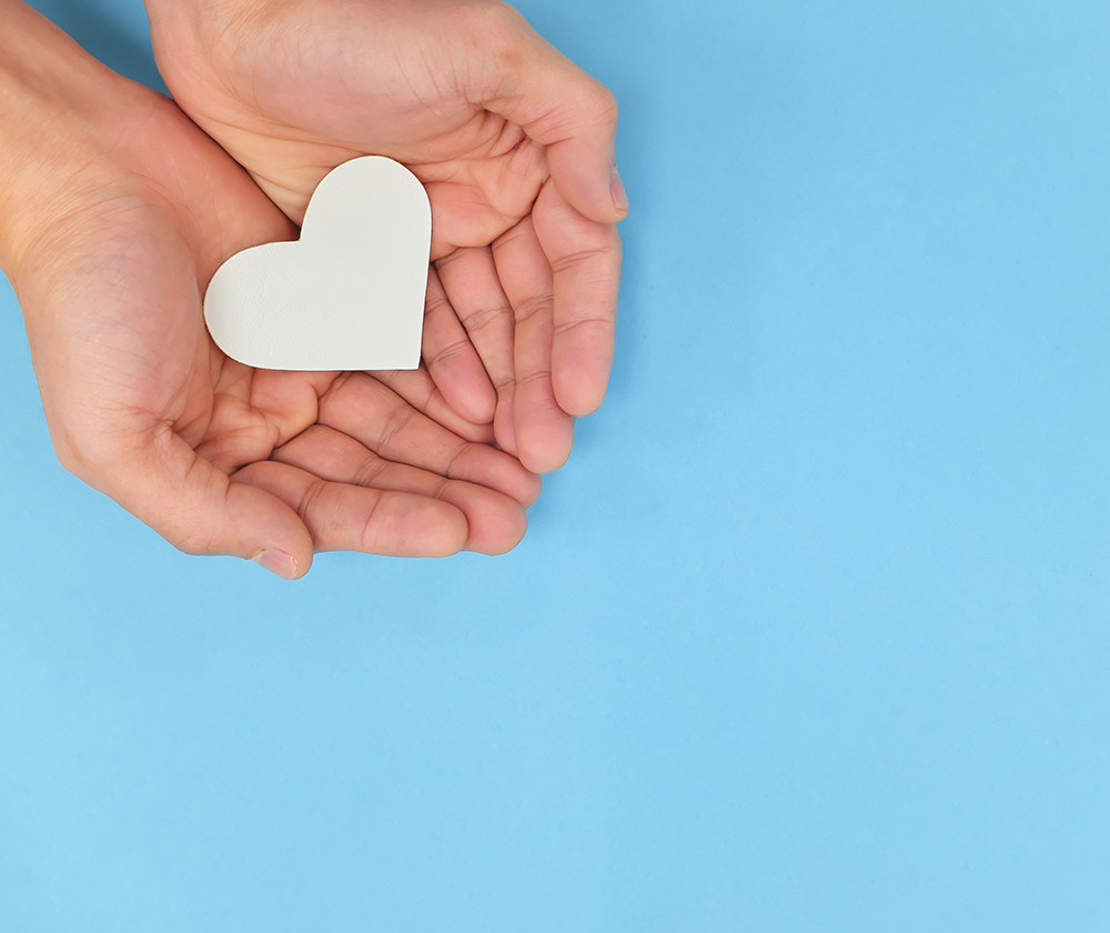 Hands holding a white heart in blue background. Charity, pure lo Hands holding a white heart in blue background. Charity, pure lo